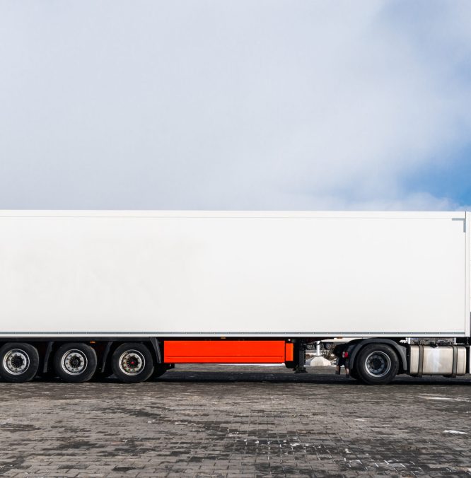 A big white truck with a white trailer standing on the countryside road in against a blue sky with clouds. Transportation concept